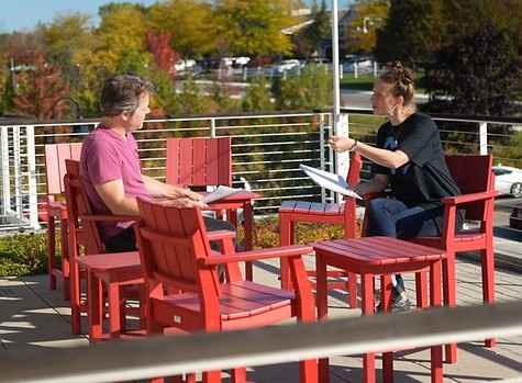 Two people sit in red chairs speaking to one another