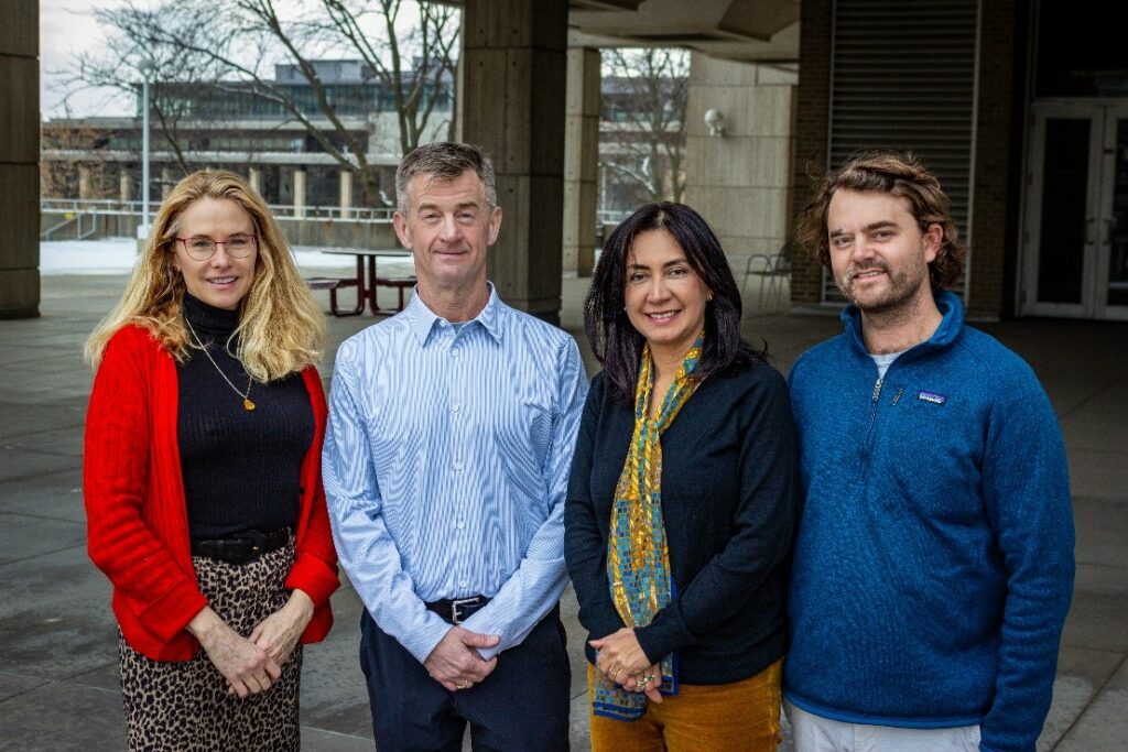 Four people smile and pose in front of a building