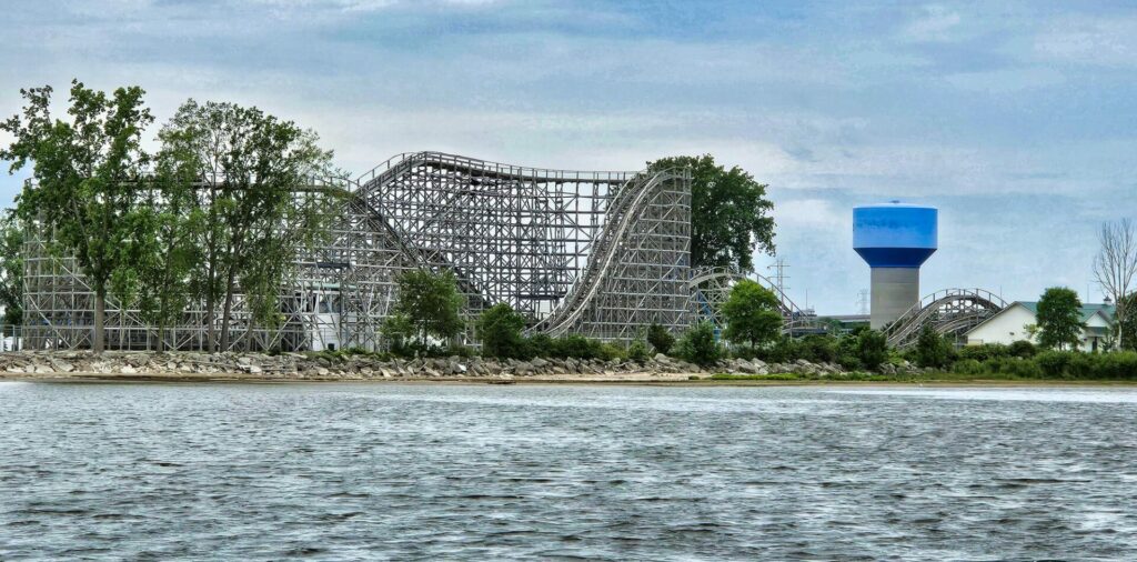 A rollercoaster and water tower along a shoreline with water in the foreground